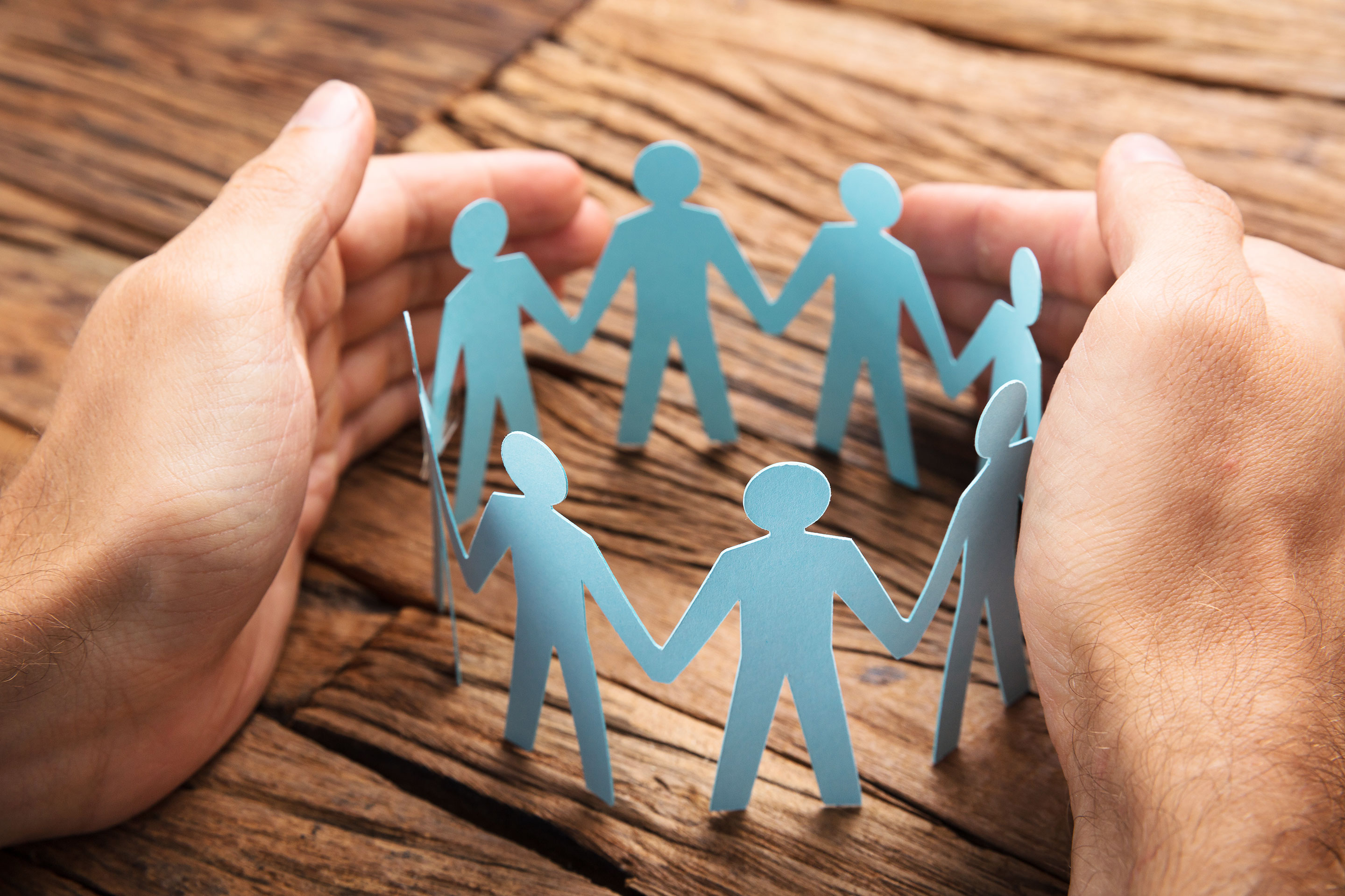 Hands surround a circular cutout of people holding hands, representing communities.