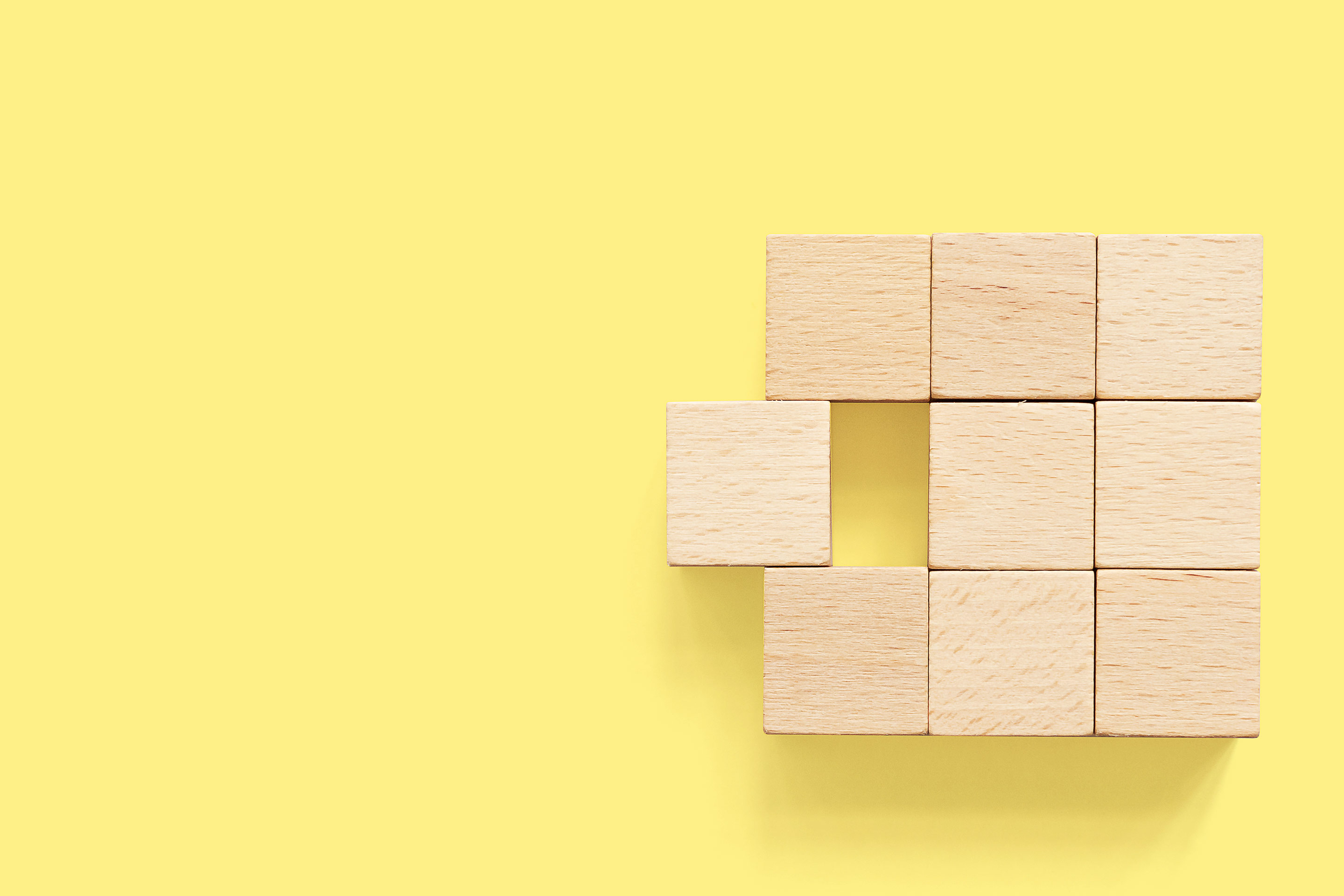 Six natural wood blocks forming a symmetrical square, with one block sliding in or out of alignment