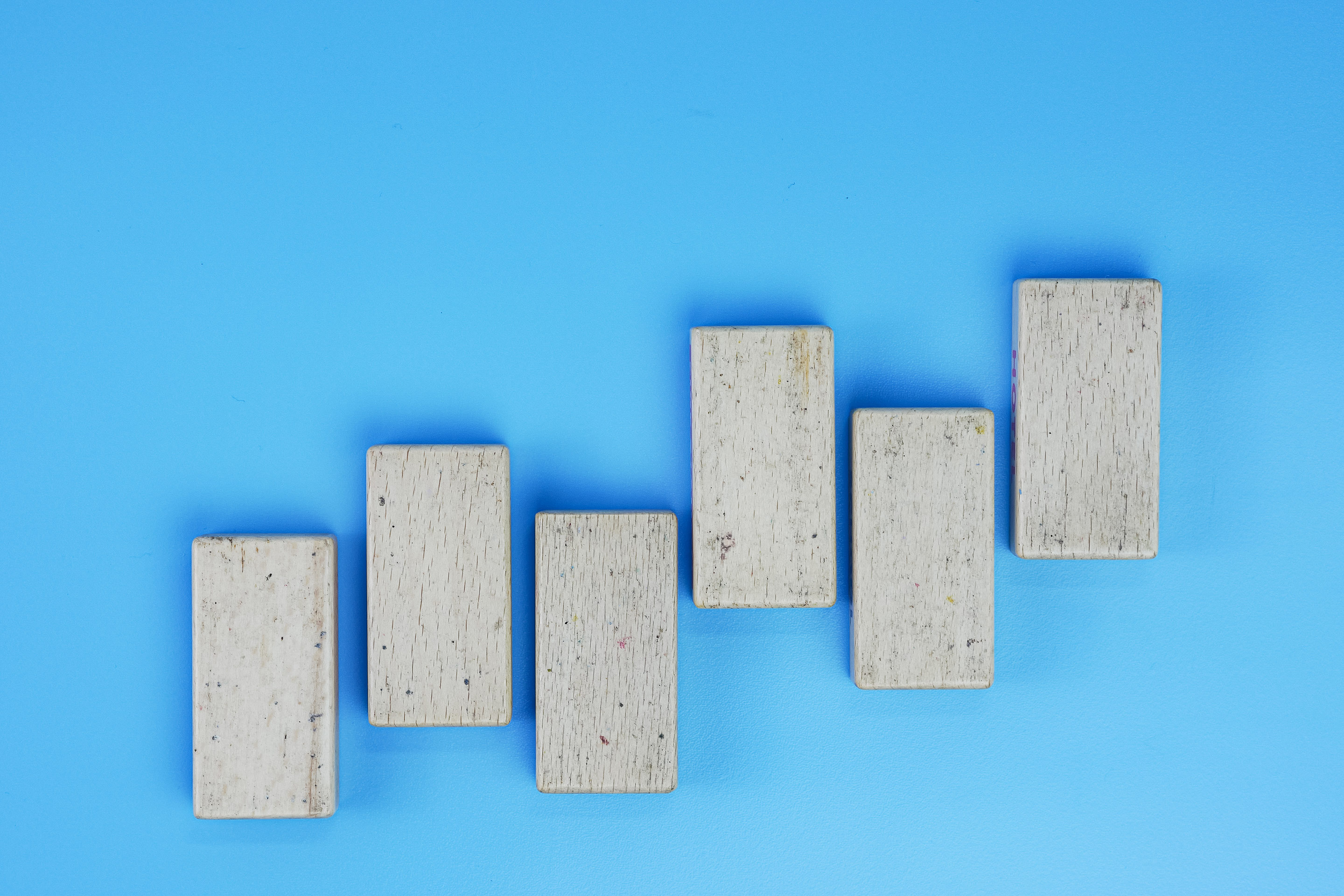 Six gray, concrete bricks are lined up in an alternating pattern that rises like bars on a graph. They stand out against a bright blue background.
