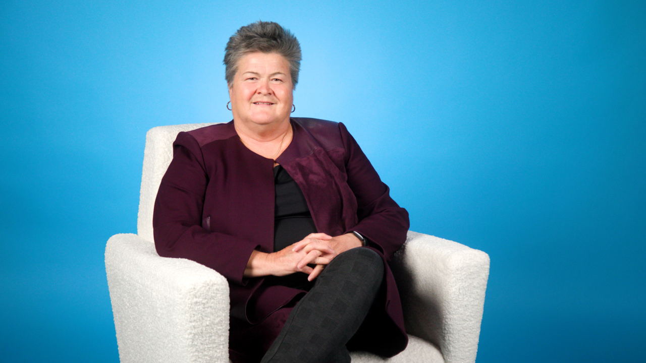 Rhonda Cook sits in a white chair with a blue background
