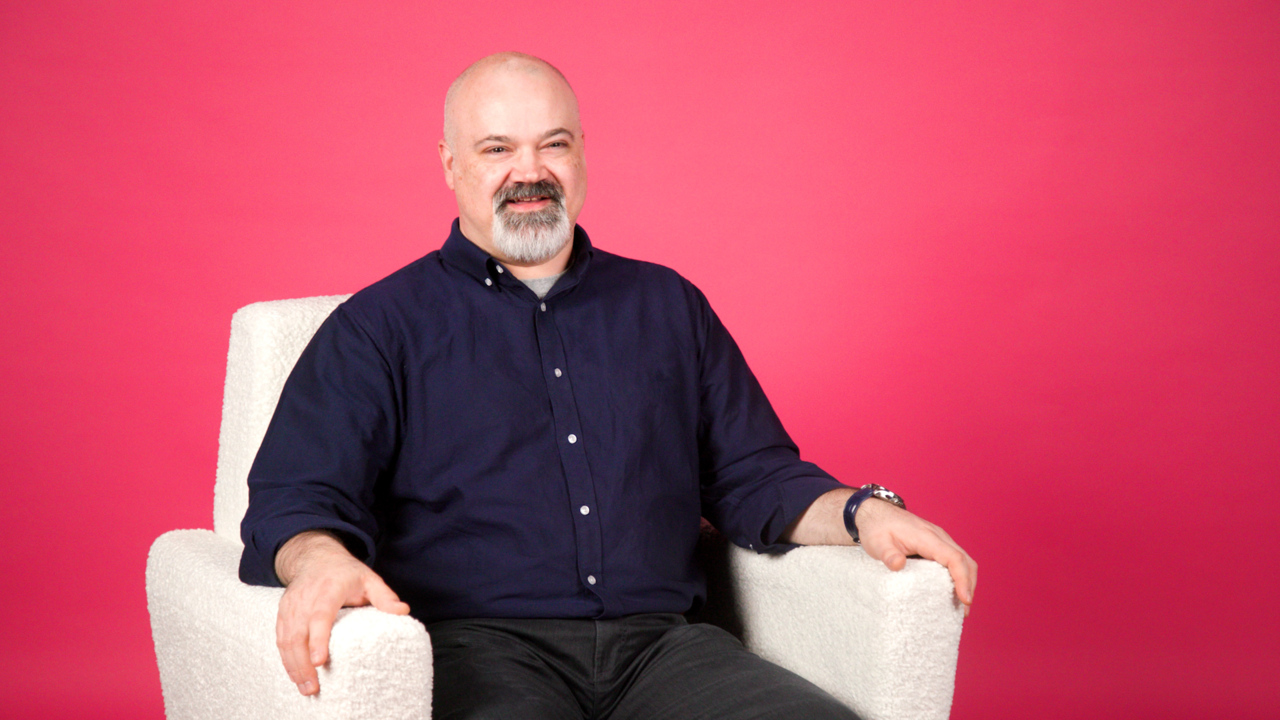 Collin Keen sits in a white chair with a pink background