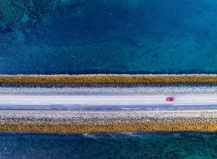 A red car drives down a single road over blue water, representing connectivity.