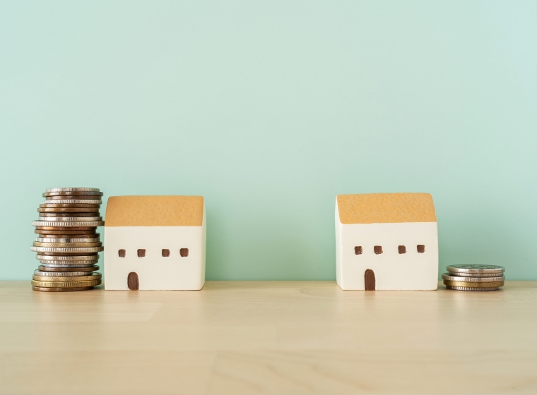 An image of two miniature houses on opposite ends, with a larger stack of coins next to one of the houses, depicting the potential benefits of financial planning