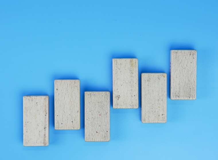 Six gray, concrete bricks are lined up in an alternating pattern that rises like bars on a graph. They stand out against a bright blue background.