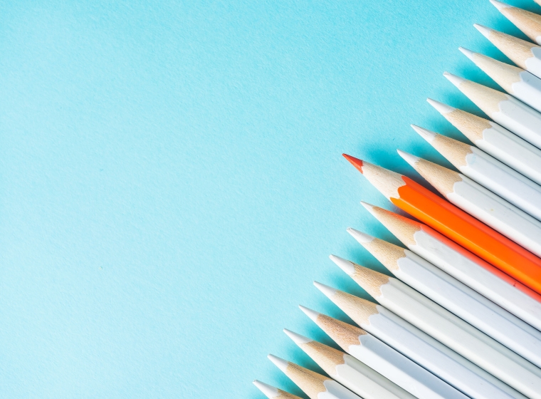 An orange pencil stands out among a row of white pencils on a blue background, representing customization.