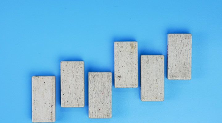 Six gray, concrete bricks are lined up in an alternating pattern that rises like bars on a graph. They stand out against a bright blue background.
