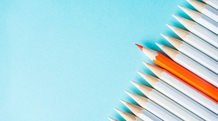 An orange pencil stands out among a row of white pencils on a blue background, representing customization.