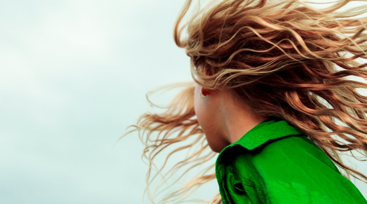 A colorful photo of a girl with red hair flying in the wind. She is wearing a bright green jacket.