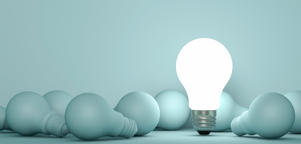 A bright lightbulb stands among a group of dark lightbulbs representing intelligence