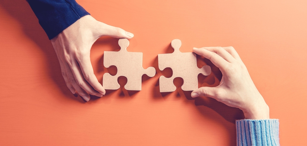 Two different individuals hold puzzle pieces that will interlock to create connectivity