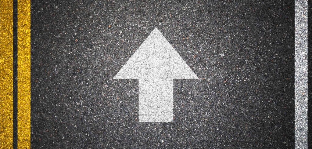 A white arrow on a dark road, pointing straight ahead.