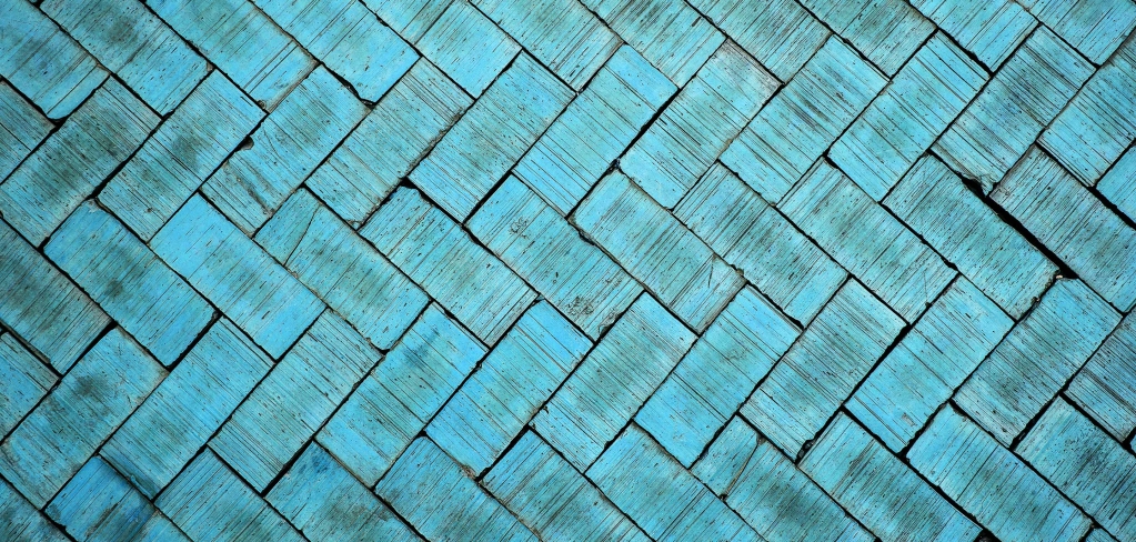 	Bright turquoise bricks, with unique markings caused by age, are laid in an eye-catching chevron pattern across the entire photo.