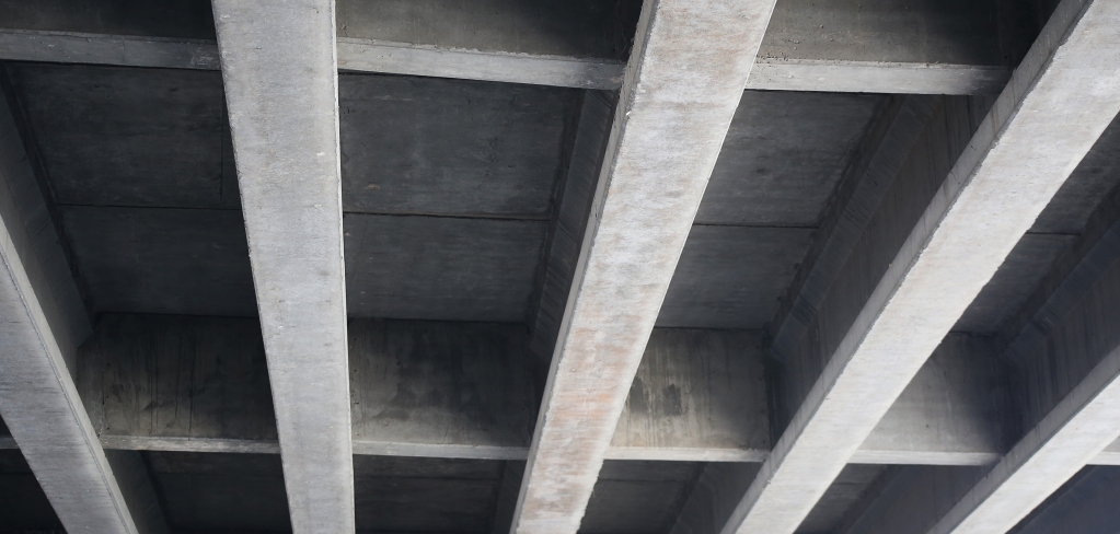 	An industrial concrete ceiling with strong, straight support beams.