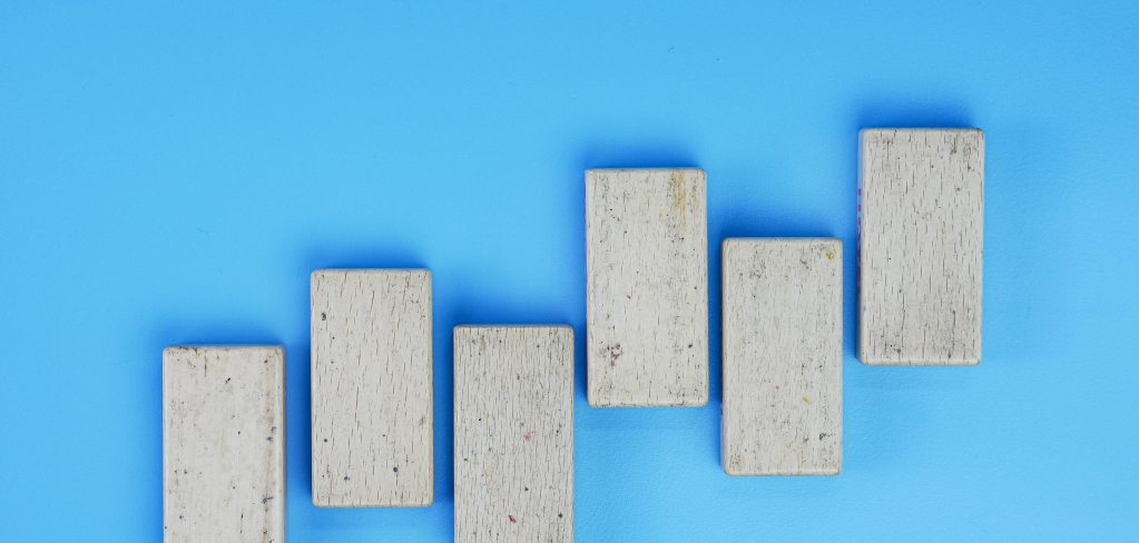 Six gray, concrete bricks are lined up in an alternating pattern that rises like bars on a graph. They stand out against a bright blue background.