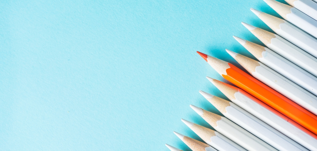 An orange pencil stands out among a row of white pencils on a blue background, representing customization.