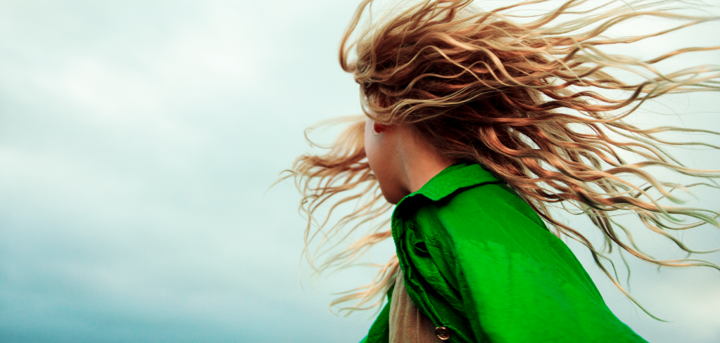 A colorful photo of a girl with red hair flying in the wind. She is wearing a bright green jacket.