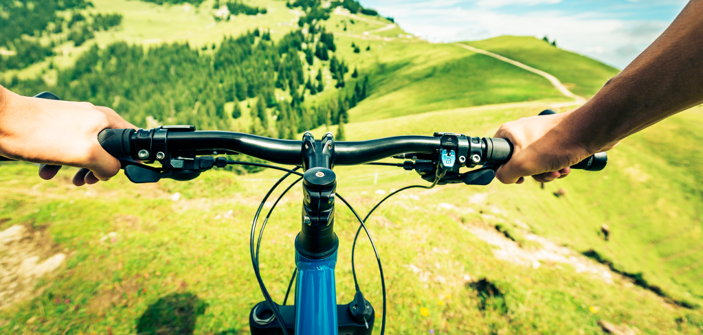 Two hands grip mountain bike handle bars-beautiful green rolling hills from the viewpoint of the rider.