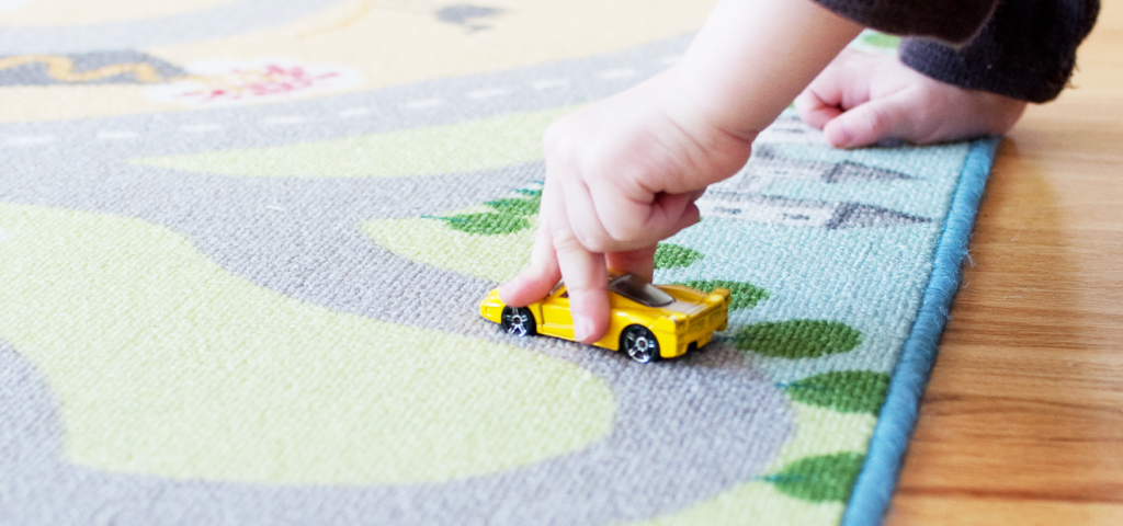 Child playing with toy car on a rug map