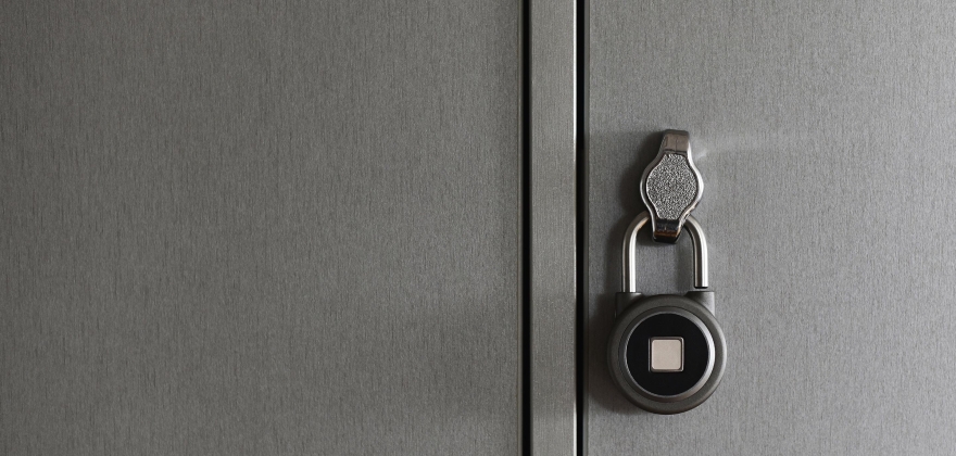 A silver and black padlock hangs on stainless steel door. There is no apparent way to open the padlock, as there is a noticeable white block where the keypad or combination would be.