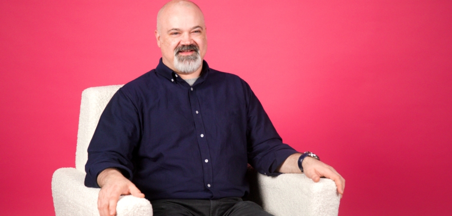 Collin Keen sits in a white chair with a pink background