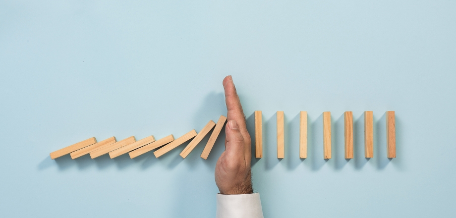 A hand blocks a line of dominoes from falling.