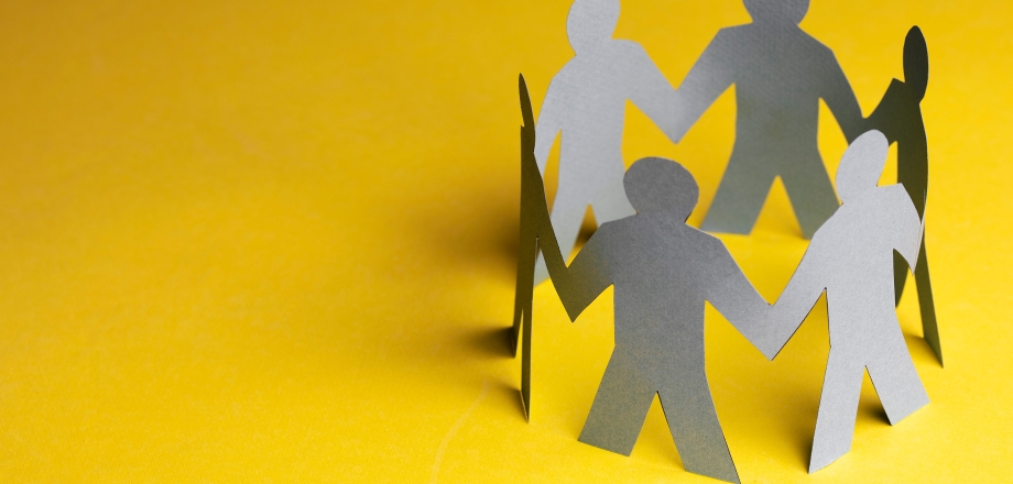 Grey paper cutouts of people hold hands on a yellow background representing ecosystem