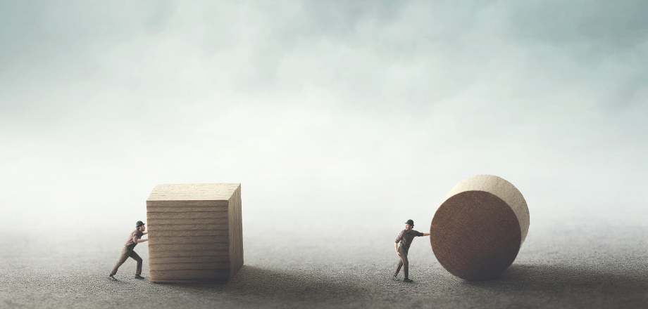 Image of one man pushing a large wooden square and another man pushing a large round circle, representing modernization