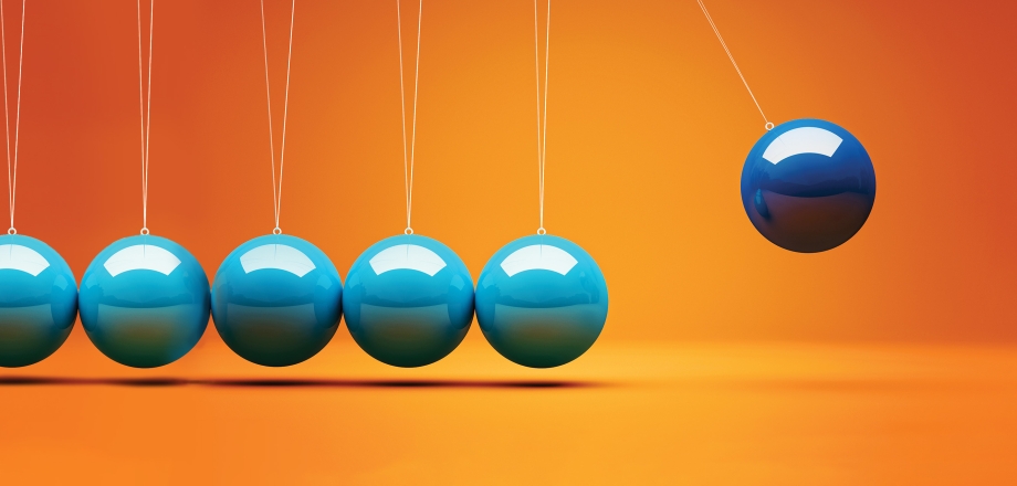 Blue and aqua kinetic balls swinging against a bright orange background, suggesting momentum