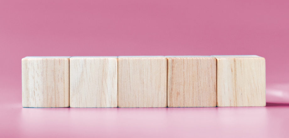 Five wooden blocks in a row on a pink background