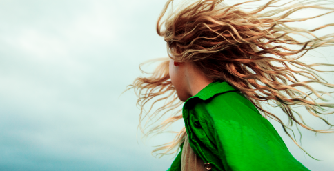 A colorful photo of a girl with red hair flying in the wind. She is wearing a bright green jacket.